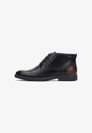 Botas de cuero negras hasta el tobillo con un acento de cuero marrón, punta redonda, cierre de cordones de seis ojales y suela plana de goma.