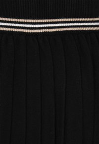 Zwarte geplooide rok met een geribbelde taillestrik en drie horizontale strepen in wit en metallic goud. Zacht, textuurstof.