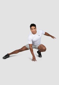 Hvit atletisk skjorte og lys grå shorts på en person i en dynamisk utfallposisjon. svarte atletiske sko med minimale detaljer. Glatt tekstur.