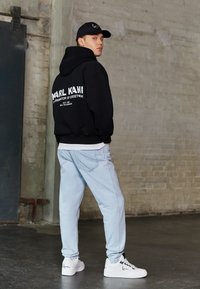 Czarna hoodie z białym logo, jasnoniebieskie dżinsy i białe sneakersy z czarnymi akcentami. Gładki, luźny krój. Prosty design i minimalne detale.