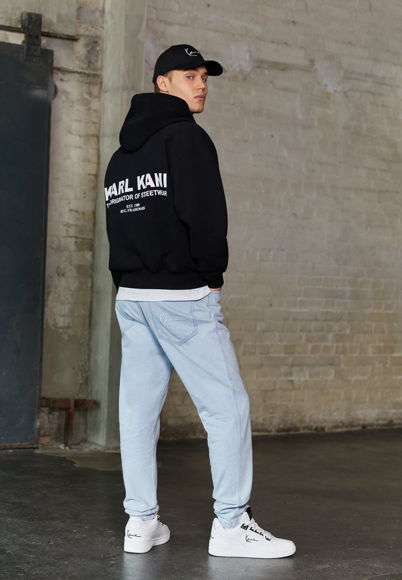 Czarna hoodie z białym logo, jasnoniebieskie dżinsy i białe sneakersy z czarnymi akcentami. Gładki, luźny krój. Prosty design i minimalne detale.