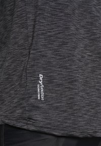 Mørkegrå stof med subtil vandret tekstur og hvid "Dryfunction Techno Fibre" logo nær sømmen, båret over sorte shorts eller leggings.