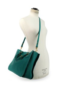Sac à main en cuir bleu sarcelle avec ferrures dorées et bandoulière, présenté sur un mannequin de couture blanc.