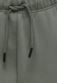 Grønne bomuldsjoggers med snor i taljen, der har kontrasterende sorte spidser og en glat overflade. Subtil syning er synlig.