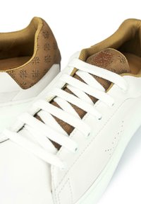 Bílé tenisky s hladkým koženým povrchem, hnědým vzorovaným semišovým podpatkem a bílými šňůrkami, které mají jemné perforace po stranách.
