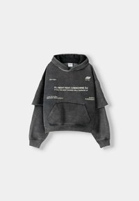 Sudadera gris extragrande con cordón, bolsillo frontal y mangas con capas. Presenta texto y gráficos blancos en el frente. Material de mezcla de algodón.