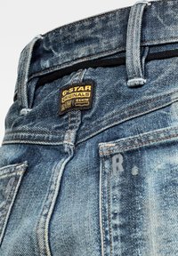 Närbild av midjan på blå denimjeans med G-Star Originals Raw Denim-märke samt synliga bältesögglor och fickor.