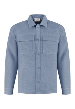 Blauwe wollen blouse met een knoopsluiting aan de voorkant, twee borstzakken en een klassieke kraag. De textuur is zacht en iets pluizig.