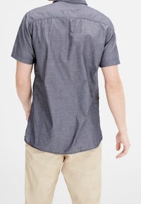 Korte mouwen shirt in donkerblauwe stof, met een kraagachting, rugplooien en een afgeronde zoom, gecombineerd met lichtbeige broeken.