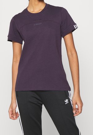 Personne portant un t-shirt Adidas violet foncé et un pantalon de survêtement Adidas noir avec des bandes blanches sur les manches et les côtés du pantalon.