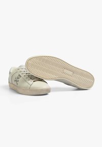 Sneaker beige con tomaia in pelle liscia, un sottile logo con teschio e ossa incrociate, e una suola in gomma strutturata con motivo a chevron.