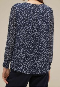 Marinebluse mit einem hellgrauen Blattmuster, langen Ärmeln mit gerafften Manschetten und einem Knopfdetail hinten. Weicher, leichter Stoff.