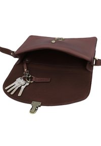 Brūna ādas plecu soma atvērta, redzams tās iekšpuse ar piesaistītu atslēgu gredzenu, kurā ir četras sudraba atslēgas.