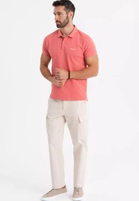 Růžová polo trička s třemi knoflíky, béžové cargo kalhoty s bočními kapsami a světle hnědé tenisky. Jednoduchý, ležérní outfit.