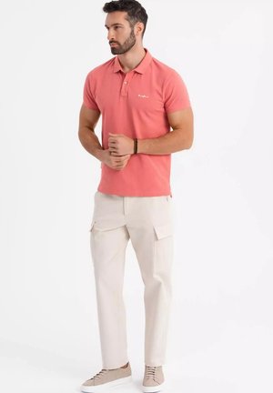 Rosa Poloshirt mit drei Knöpfen, beigefarbene Cargo-Hose mit Seitentaschen und hellbraune Sneaker. Schlichte, lässige Outfit.