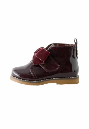 Glanzige donker bordeaux enkellaars met een grote zachte stoffen strik bovenop en een lichtbruine rubberen zool.