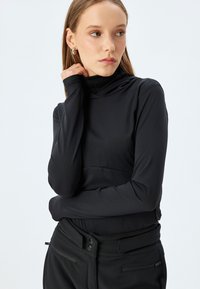 Zwart lange mouw top met een hoge hals; glad, rekbaar materiaal; aansluitend ontwerp; gecombineerd met high-waisted broek met een platte tailleband.
