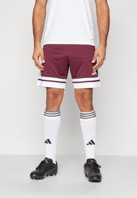Bordeaux atletische shorts met witte strepen aan de zoom, gedragen met zwarte voetbalschoenen en zwart-wit gestreepte sokken.