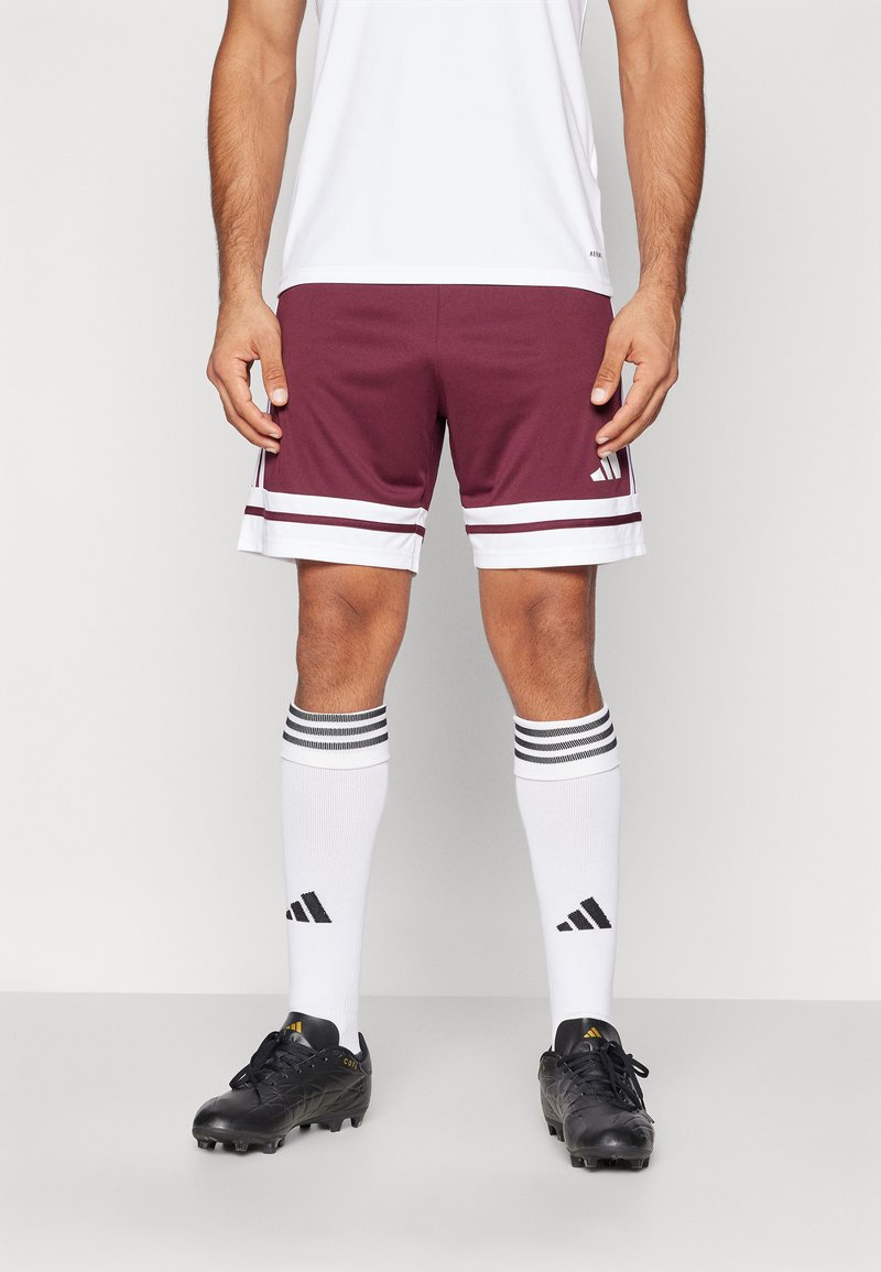 Bordeaux atletische shorts met witte strepen aan de zoom, gedragen met zwarte voetbalschoenen en zwart-wit gestreepte sokken.
