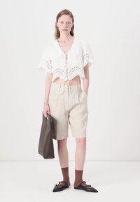 Hvit bluse med korte ermer, broderie anglaise-detaljer og knytebånd foran, kombinert med lyse beige shorts og en mørk totebag.