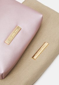 Két táska: az egyik rózsaszín műbőr arany logóval, a másik bézs texturált anyagból készült, mindkettő téglalap alakú arany díszítéssel rendelkezik.