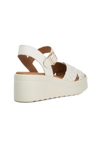 Witte wedge sandaal met een bovenkant van gevlochten leder, verstelbare gesp, chunky zool en een tekstuur voetbed. Zijaanzicht toont een uitgesneden ontwerp.