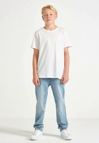 Vit bomullst-shirt med korta ärmar, kombinerad med blå jeans och vita sneakers. Enkel design och avslappnad passform.