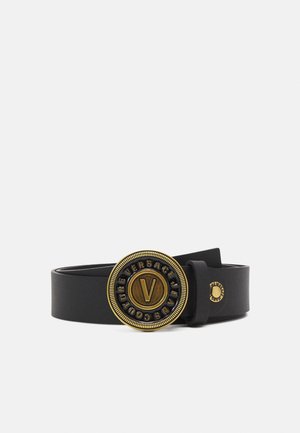 Czarny skórzany pasek z okrągłą złotą klamrą z literą „V” na środku i napisem „Versace Jeans Couture” na krawędzi.