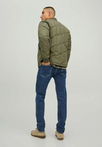 Chaqueta acolchada verde oliva con cuello alto, combinada con vaqueros azules. La chaqueta presenta un patrón de diamantes y puños acanalados.