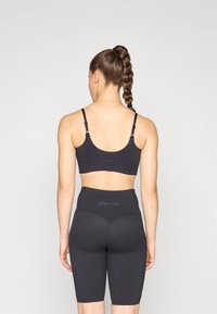 Sujetador deportivo negro con tirantes ajustables y logo; pantalones cortos de ciclista negros de cintura alta con diseño sin costuras y logo en la parte trasera.