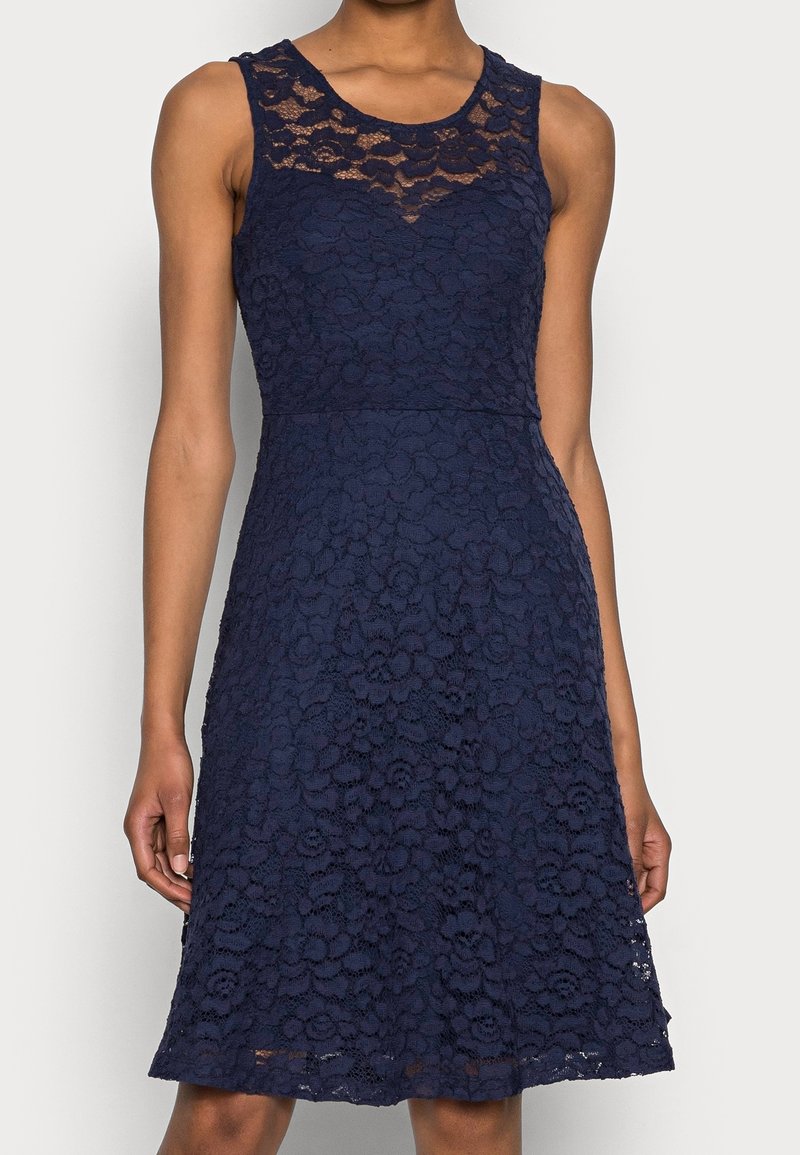 Marinblå ärmlös spetsklänning med blommönster, figursydd överdel och utsvängd kjol, med en ellypsformad spetskrage och textur.