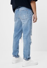 Ljusblå slitna jeans med lös passform, fransiga fållar och subtil blekning, kombinerade med vita sneakers.