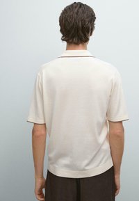 Polo a maniche corte in cotone beige chiaro, con colletto classico e dettagli in marrone a contrasto lungo le maniche e l'orlo.