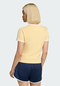 Žlté tričko s krátkym rukávom s bielym lemom na golieri a rukávoch, skombinované s tmavomodrými šortkami s bielymi detailmi.
