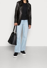 Blazer de cuero negro sobre un suéter negro, jeans anchos de tiro alto en azul claro y zapatillas negras con suelas blancas. Sosteniendo un bolso negro.