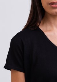 T-shirt nera a maniche corte con scollo a V, realizzata in materiale morbido. La vista ravvicinata mette in risalto il collo e la texture uniforme.