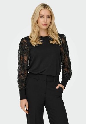 Schwarzes Langarmoberteil mit Blumen-Spitzenärmeln, gerippten Ärmelbündchen und Rundhalsausschnitt, kombiniert mit schwarzen maßgeschneiderten Hosen.