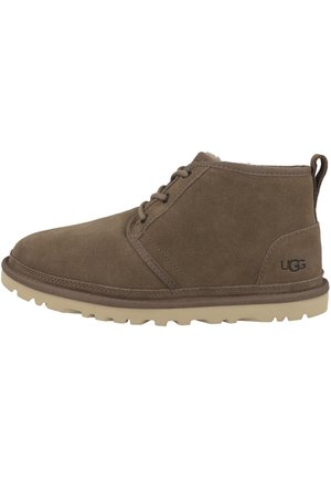 Botas de ante marrón hasta el tobillo con cordones, suela de goma y logo de UGG. Punta redonda, superficie texturizada y interior acolchado para mayor comodidad.
