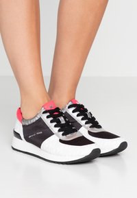 Svartvita sneakers med nät- och släta texturer. Utrustade med silverdetaljer, rosa krage, svarta snören och ett mönstrat sidopanel.