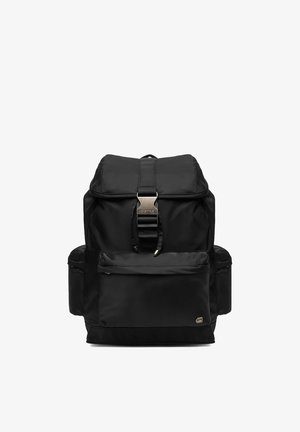 Czarny plecak z klapką na górze, przednią kieszenią na zamek, bocznymi kieszeniami oraz centralnym metalowym zapięciem na klamrę. Kompaktowy i funkcjonalny design.