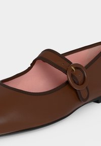 Chaussure plate Mary Jane marron avec bout arrondi, boucle circulaire décorative et doublure intérieure rose clair.