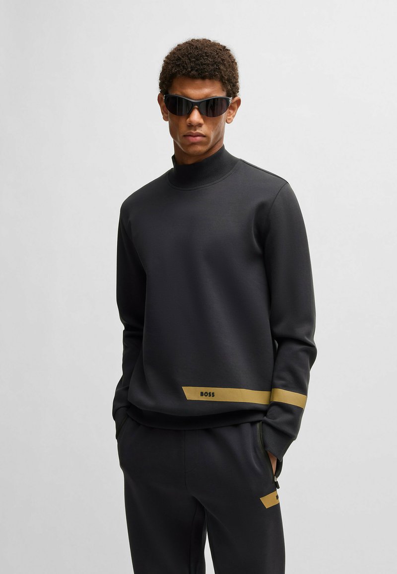 Svart sweatshirt med hög krage, prydd med ett guld horisontellt rand och "BOSS"-logotypen på den nedre framsidan. Tillverkad av ett slätt, strukturerat tyg.