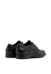 Pantofi negri din piele cu un finisaj texturat, vârf rotunjit și șase găuri pentru sireti. Talpă plată din cauciuc, design minimalist și margini netede.