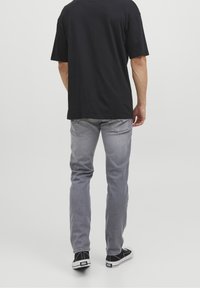 Vaqueros grises de corte recto, con un desvanecido sutil y detalles de costuras visibles, combinados con una camiseta negra de manga corta y zapatillas negras.