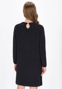 Robe bleu marine à manches longues en tissu texturé avec une découpe en forme de goutte d'eau dans le dos. Silhouette simple et droite avec un col rond.