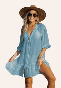 Robe bleue claire à boutons avec des manches et un ourlet à volants. Tissu transparent avec une coupe fluide, comportant des fentes latérales pour un mouvement supplémentaire.