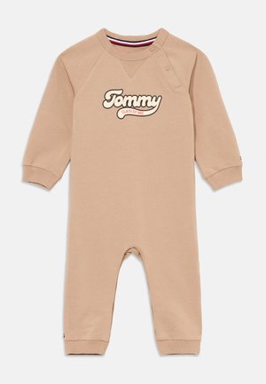 Beige babyspringdragt med lange ærmer og ribbede manchetter, som har et fremtrædende "Tommy" logo og trykknaplukning ved skulderen.
