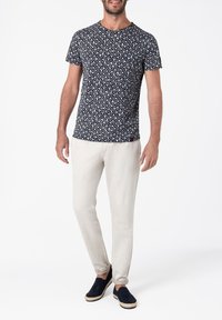 Kurzes T-Shirt mit Marine-Muster und weißen geometrischen Designs, kombiniert mit hellbeigen Hosen und marineblauen Slippern mit Seil-Akzenten.