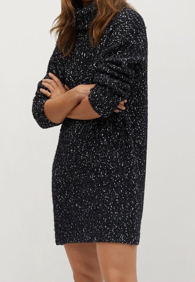 Robe-pull en maille tachetée noir et blanc avec un col montant, des manches amples et un tissu texturé, atteignant la mi-cuisse.