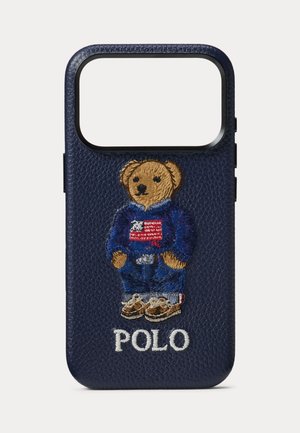 Husă pentru telefon din piele bleumarin cu un ursuleț brodat care poartă un pulover albastru cu steagul american, iar dedesubt este brodat cuvântul „POLO”.
